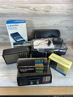 Overview of vintage electronics lot including boxed cassette recorders, calculator, radio, cords and cases.