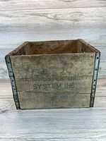 Front view of the wooden crate showing printed Manchester Dairy System branding and metal reinforcements on corners.