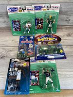 Top view of seven new sealed sports action figures and sets including Starting Lineup football and basketball figures, NFL Maps set, and Air Shot figure.