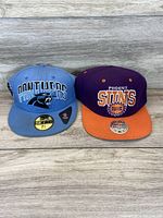 Front view of Carolina Panthers and Phoenix Suns hats side by side on wooden surface