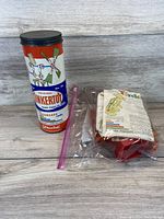 Clear view of vintage Original Tinkertoy metal tube container with colorful label and black lid, standing upright on wooden background.