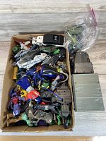 Box filled with vintage robot and action figure toys in bright colors including blue, red, green, white and gray.