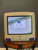 Front view of iMac G3 powered on displaying Mac OS 8.6 welcome screen.