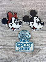 Three vintage Disney magnets: Minnie Mouse, Mickey Mouse, EPCOT Center logo on wood surface