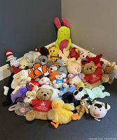 Photo of the entire lot showing approximately 27 assorted vintage plush toys arranged in a corner against dark walls.