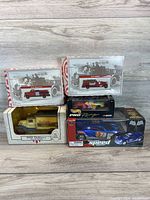 Front view of all toy vehicles in original packaging showing both fire trucks, delivery truck bank, and die-cast NASCAR cars.