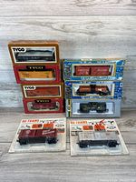 Shot of two columns of boxed and blister packed HO scale toy train cars. Left column shows four Tyco boxed cars; right column shows two blue boxed cars and two blister packed cars.