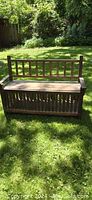 Front view of the antique wooden bench showing vertical slats in the backrest and a solid wooden seat in natural outdoor lighting.