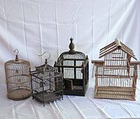 Front view of four traditional bird cages arranged side by side showing different styles and sizes.