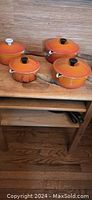 Full view of four flame orange Le Creuset sauce pans with lids on wooden table.