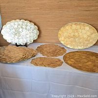 Photo showing the entire set of 25 Capiz mother of pearl placemats including the large scalloped round, medium round, small round, and large oval placemats with gold trim.