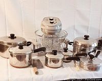 Lot overview showing various stainless steel pots and pans with black handles and lids alongside an early model air fryer with glass bowl.