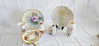 Photo showing the full assortment of six porcelain items on white fabric background under natural light, clear detail of floral paintings and shapes