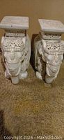 Pair of ivory white porcelain elephant sculptures with detailed carvings and flat square tops, positioned side by side on carpet.
