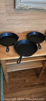Three cast iron skillets displayed on a wooden surface, including the Wagner 1891 pattern skillet showing handle and general shape.