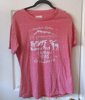 Full front view of the light red Banff National Park T-shirt on hanger against door.