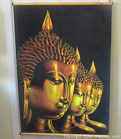 Front view of a large black velvet wall hanging with three golden Buddhas in profile, showing head and shoulders with detailed hair and faces.