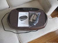 Eilison vibration plate on beige couch with user manual and wrapped arm and leg bands on top