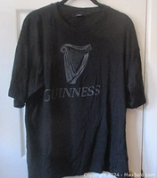 Full view of black Guinness t-shirt with harp logo and text on front.