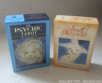 Two John Holland oracle deck boxes side by side, Psychic Tarot in blue and Spirit Messages in beige with visible titles and box art.