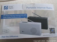 Front of the original product box showing Ocean Digital WR-26 Portable Internet Radio in black and white variants with text on wireless internet connection, DAB+/FM, and Bluetooth features.