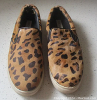 Top view of pair of Steve Madden loafers showing tan cow hair uppers with black animal print spots and white soles.