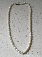 Full view of a vintage freshwater pearl necklace arranged flat on a speckled surface showing the entire length and clasp.