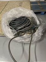 Coiled black garden hose laid inside plastic wrapping on a wooden pallet surface.