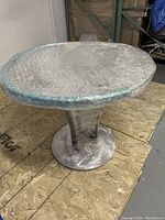 Photo of a glass coffee table with circular top and wrapped in plastic film showing metal pedestal base