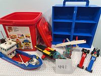 Lot overview showing assembled LEGO boat, seaplane, dragsters, loose pieces, red LEGO bucket and blue storage case.