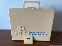 Closed view of the beige hard plastic carrying case with Fisher Price Medical Kit logo and embossed design showing the case exterior and handle.