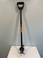 Full view of the Fiskars weed removal tool showing the long black handle with orange accents and D-shaped grip.