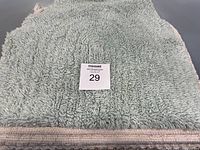 Photo showing a single folded light gray thick shaggy rug with a lot number on top.