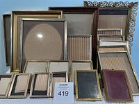 Front view of a collection of assorted vintage picture frames arranged upright, showing the variety of shapes and sizes including a large ornate frame and an oval mat frame.