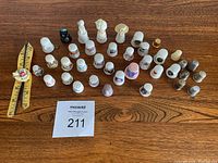 Photo showing 44 assorted thimbles arranged on a wooden surface including porcelain and metal ones with diverse decorative patterns and colors.