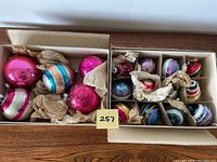 Wide box view showing larger pink and striped glass ornaments cushioned with tissue paper