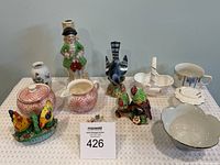 Overview of vintage figurines and china on table, including several bird figurines, bowls, and a standing male figurine