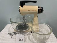 Front view of Sunbeam Mixmaster with two glass bowls and metal attachments in front, showing the unit and its accessories.