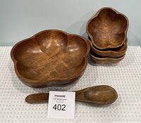 Photo showing set of one large bowl, three small bowls stacked, and a wooden spoon on a neutral surface.
