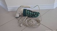 Side view of a white Bissell handheld vacuum with green leaf-patterned fabric dust bag and a power cord laid out.