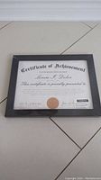 Front view of a black frame with a certificate of achievement placeholder inside, showing generic text and a gold seal.
