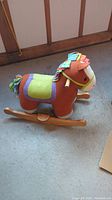 Side view of the colorful plush rocking horse with wooden base and handles