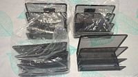 Three black metal mesh office folder holders stacked together, two wrapped in plastic, one unpackaged showing multiple compartments