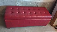 Front angled view of red leather storage bench showing tufted top and vertical stitched panels on sides