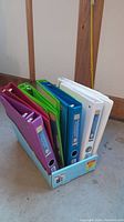 Side view of 13 binders in multiple colors placed inside a box.