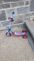 Side angle view of blue and red children's scooter featuring Spiderman graphics on the foot deck, handlebar pad, and frame. The scooter has three wheels for stability.