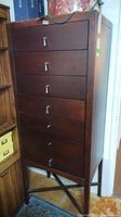 Front view of tall wooden cabinet showing six drawers and silver metal pulls, some pulls damaged or missing
