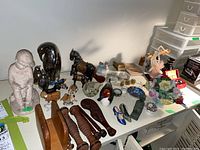 Overview photo showing all items on a table, including statuette, metal figurines, wooden items, china flowers, and decorative shoes.