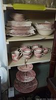 Top shelf showing two stacks of red transferware plates and bowls plus one cream Woodland bowl