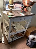 Side view of white kitchen cabinet showing metal top and open shelves below with various removed contents.